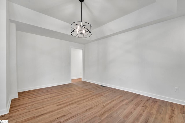 empty room featuring a raised ceiling, baseboards, light wood finished floors, and a chandelier