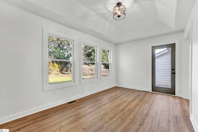 spare room featuring a raised ceiling, light wood-style flooring, baseboards, and visible vents