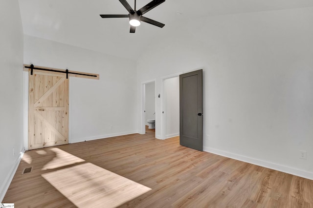 empty room featuring ceiling fan, a barn door, baseboards, and wood finished floors