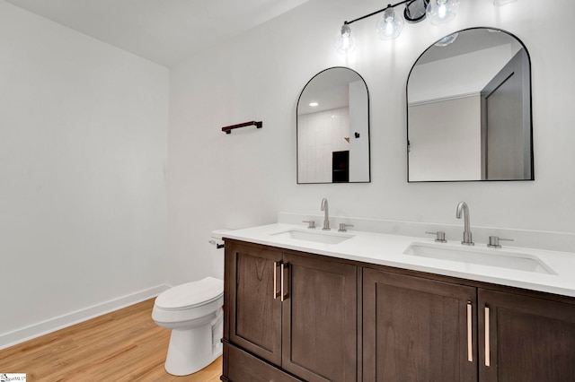 bathroom with toilet, wood finished floors, baseboards, and a sink