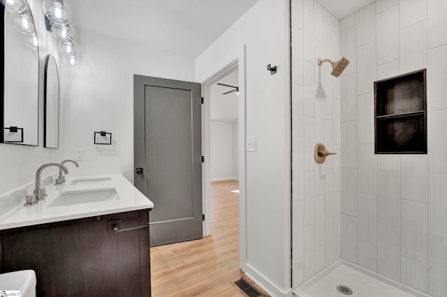 full bathroom featuring visible vents, a sink, wood finished floors, double vanity, and tiled shower