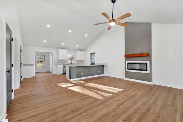 unfurnished living room featuring a ceiling fan, baseboards, high vaulted ceiling, a fireplace, and light wood-style floors