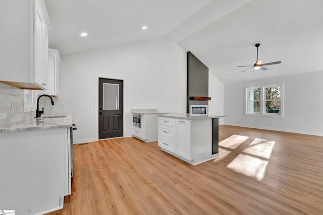 kitchen with light wood finished floors, vaulted ceiling, white cabinetry, and a sink