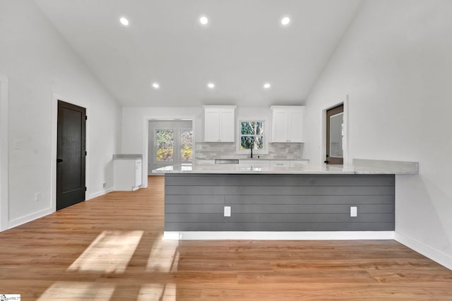 kitchen featuring high vaulted ceiling, backsplash, a peninsula, white cabinets, and light wood finished floors