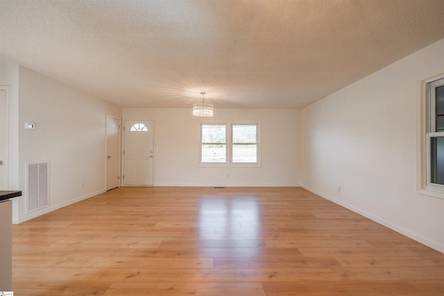 interior space featuring visible vents, a textured ceiling, a notable chandelier, and light wood finished floors