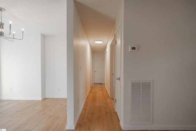 hallway with baseboards, visible vents, light wood finished floors, attic access, and a notable chandelier