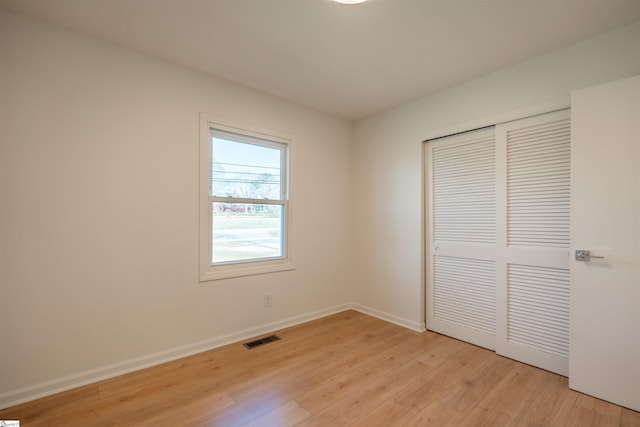 unfurnished bedroom with light wood-style flooring, baseboards, visible vents, and a closet