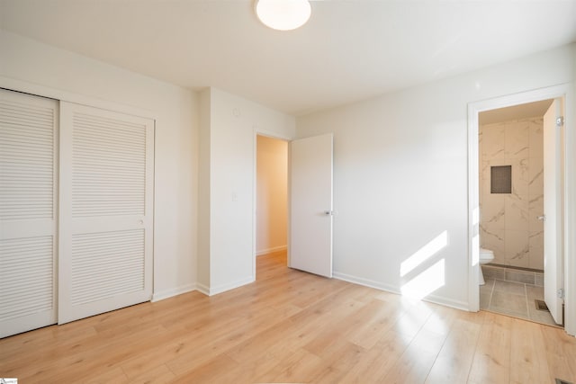 unfurnished bedroom featuring a closet, ensuite bath, light wood-type flooring, and baseboards