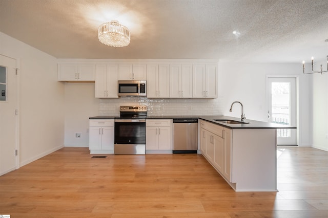 kitchen with a notable chandelier, a sink, dark countertops, stainless steel appliances, and a peninsula