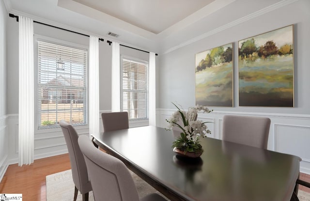 dining space featuring a tray ceiling, a decorative wall, light wood-style floors, and visible vents