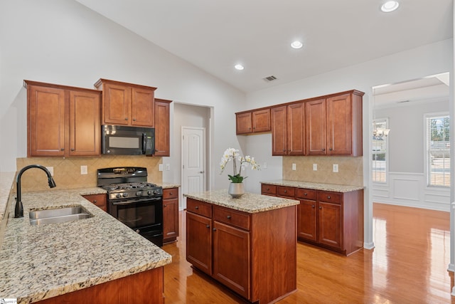 kitchen with visible vents, black appliances, a sink, light stone counters, and lofted ceiling