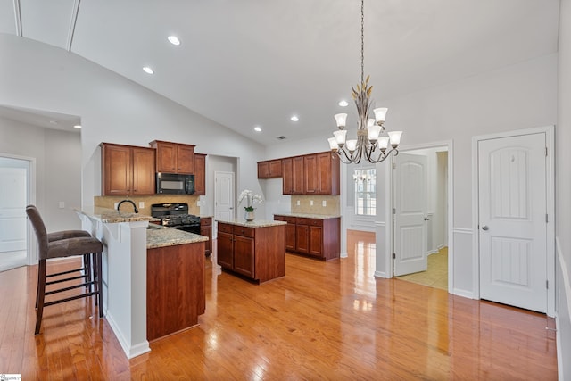 kitchen with black appliances, light wood-style flooring, a peninsula, brown cabinetry, and light stone countertops