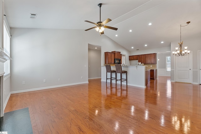 unfurnished living room featuring visible vents, ceiling fan with notable chandelier, light wood-style floors, and vaulted ceiling