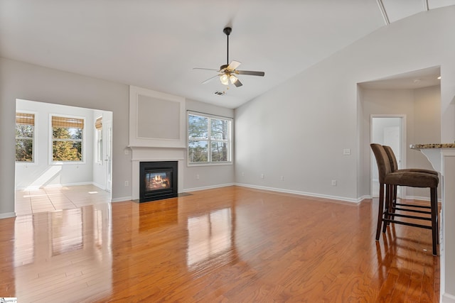 living room with light wood finished floors, baseboards, ceiling fan, a fireplace with flush hearth, and vaulted ceiling