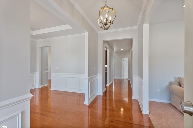 hallway with a chandelier, a wainscoted wall, ornamental molding, wood finished floors, and a decorative wall