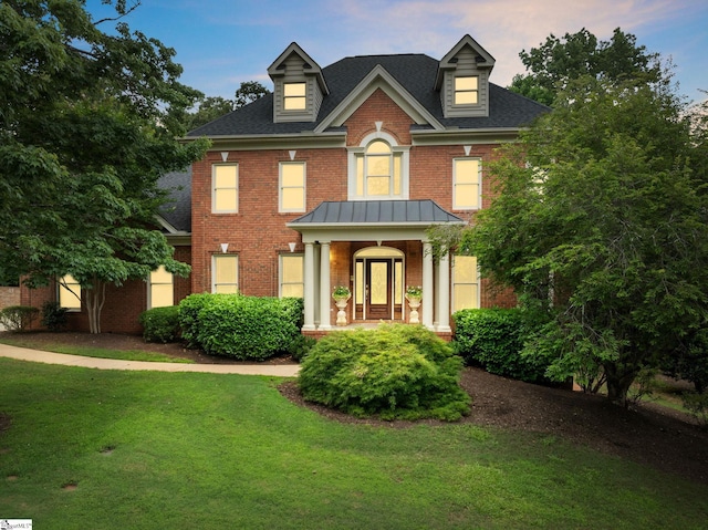 colonial-style house with brick siding, a front yard, roof with shingles, metal roof, and a standing seam roof