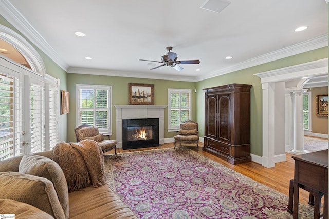 living room featuring a fireplace with flush hearth, ornamental molding, light wood finished floors, decorative columns, and baseboards