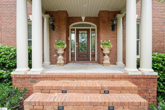 view of exterior entry with a porch and brick siding