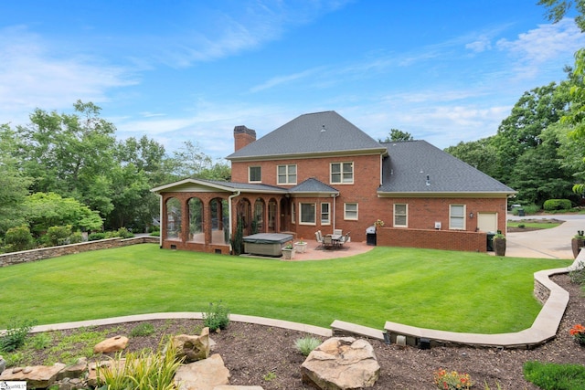 back of house featuring a patio, an attached garage, a chimney, a lawn, and brick siding