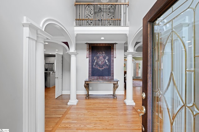 entrance foyer with decorative columns, arched walkways, baseboards, and wood finished floors