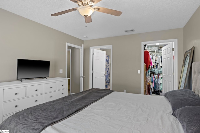 bedroom featuring visible vents, a walk in closet, ceiling fan, a closet, and a textured ceiling