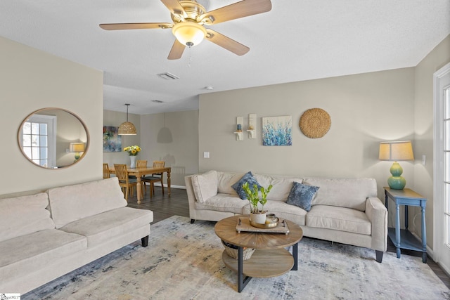 living room with ceiling fan, visible vents, baseboards, and wood finished floors