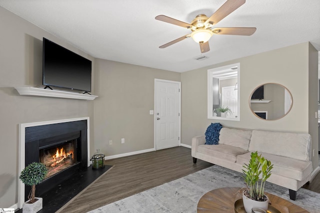 living area featuring visible vents, a fireplace with flush hearth, wood finished floors, baseboards, and ceiling fan