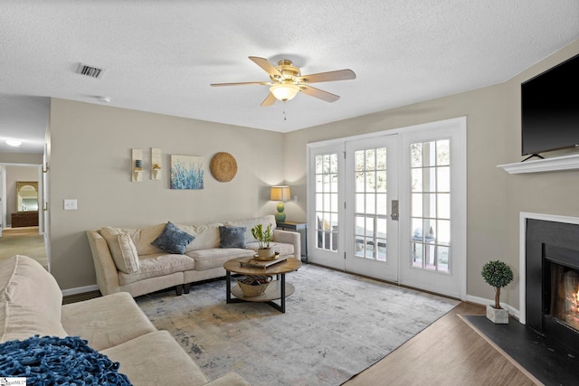 living area featuring baseboards, ceiling fan, wood finished floors, a glass covered fireplace, and a textured ceiling