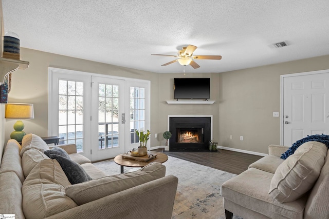 living area with visible vents, a textured ceiling, a warm lit fireplace, wood finished floors, and baseboards