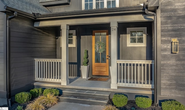 view of exterior entry featuring a porch, roof with shingles, and board and batten siding