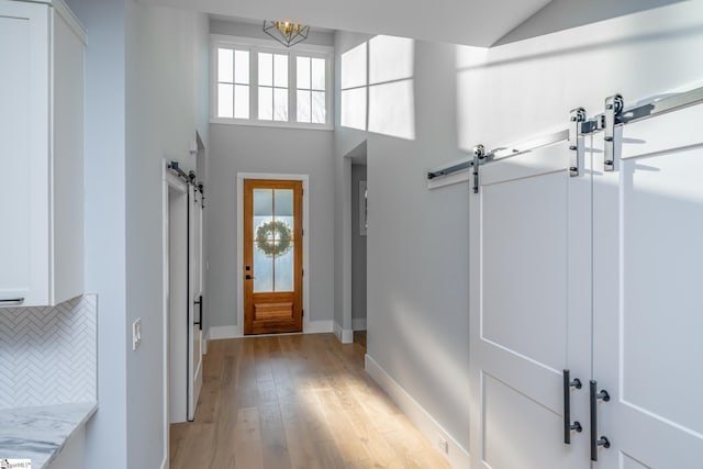 foyer with baseboards, light wood-type flooring, a barn door, a high ceiling, and an inviting chandelier