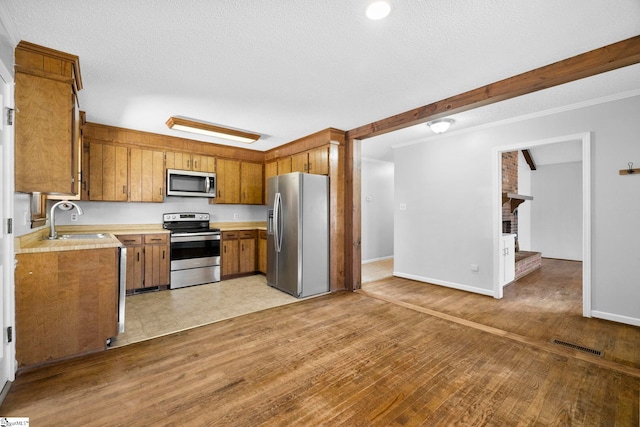 kitchen with visible vents, a sink, stainless steel appliances, light wood-style floors, and brown cabinetry