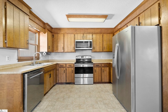 kitchen with brown cabinetry, a sink, light countertops, appliances with stainless steel finishes, and a textured ceiling