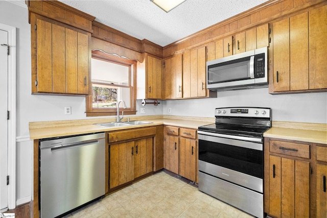 kitchen with light countertops, brown cabinets, stainless steel appliances, a textured ceiling, and a sink