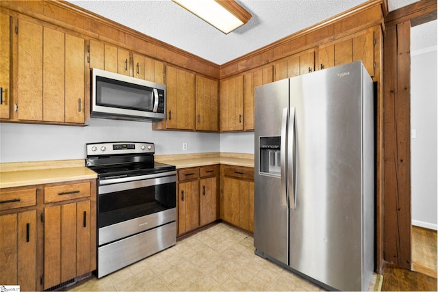 kitchen featuring light floors, light countertops, brown cabinets, appliances with stainless steel finishes, and a textured ceiling