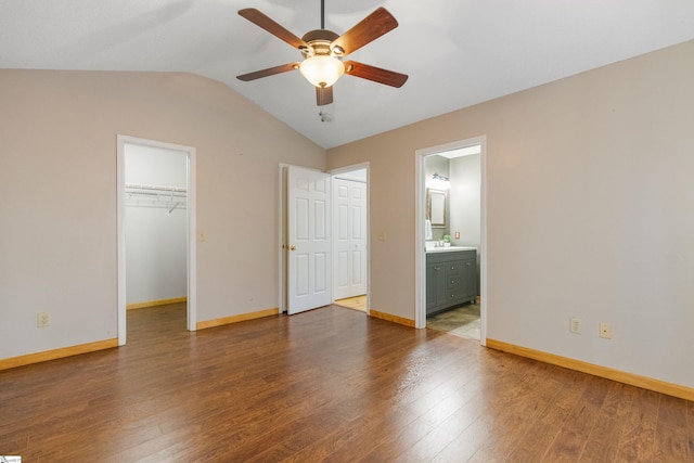 unfurnished bedroom featuring wood finished floors, baseboards, lofted ceiling, a walk in closet, and connected bathroom