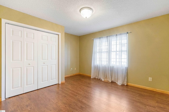 unfurnished bedroom with a closet, a textured ceiling, baseboards, and wood finished floors