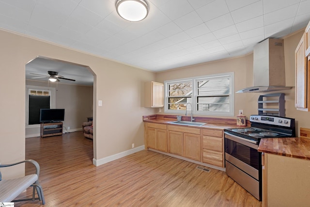 kitchen with butcher block countertops, stainless steel electric range, arched walkways, wall chimney exhaust hood, and a sink