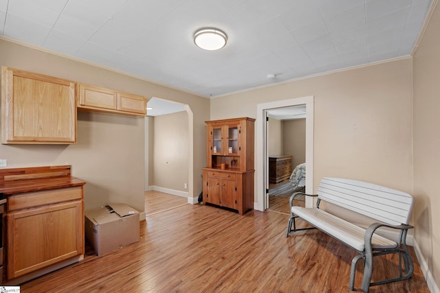 kitchen with baseboards, light wood-style flooring, arched walkways, ornamental molding, and light brown cabinetry