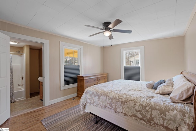 bedroom featuring a ceiling fan, baseboards, ensuite bath, light wood-style flooring, and ornamental molding