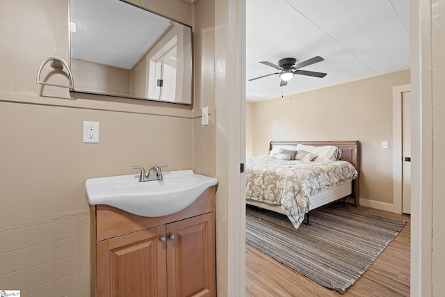 bedroom featuring a ceiling fan, baseboards, light wood finished floors, and a sink