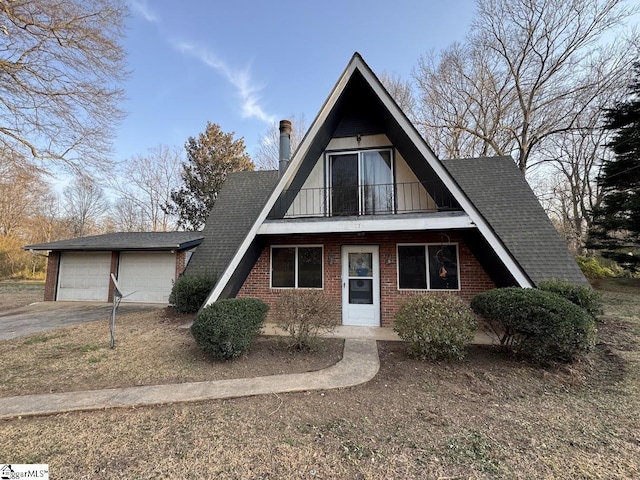 a-frame home with a balcony, a shingled roof, concrete driveway, a garage, and brick siding