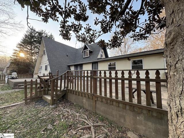 view of side of home with a shingled roof, stucco siding, and a wooden deck