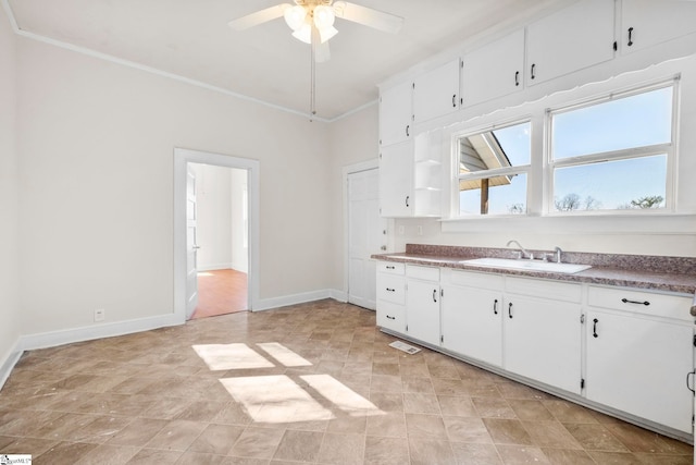 kitchen featuring a ceiling fan, baseboards, a sink, white cabinets, and crown molding