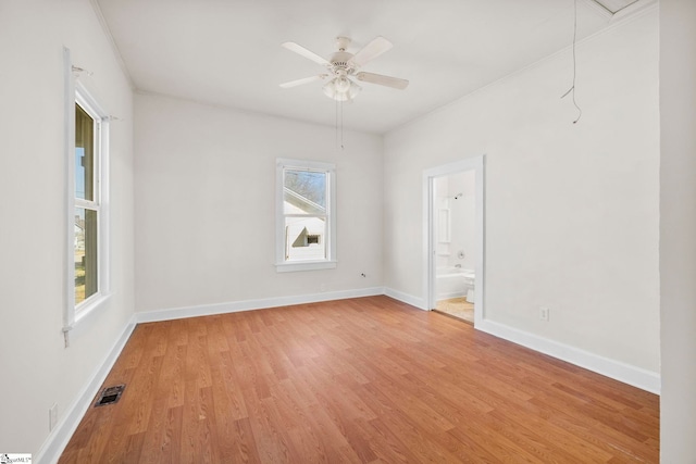 spare room with visible vents, baseboards, attic access, light wood-style flooring, and a ceiling fan