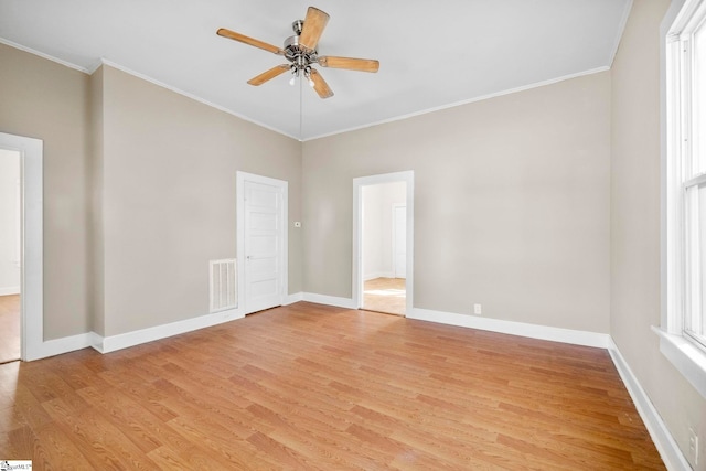 empty room with light wood finished floors, visible vents, ceiling fan, baseboards, and ornamental molding