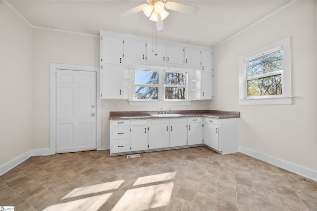 kitchen with crown molding, white cabinets, baseboards, and a sink