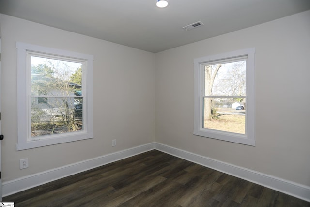 empty room with dark wood finished floors, visible vents, plenty of natural light, and baseboards