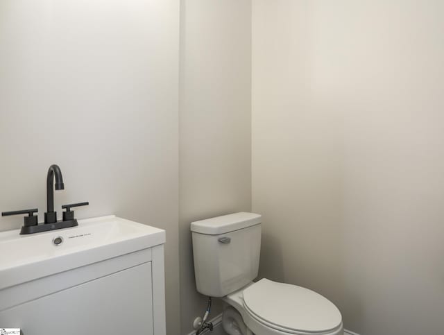 half bathroom with baseboards, toilet, and vanity