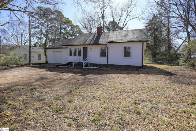 back of property with driveway, entry steps, roof with shingles, an attached garage, and a chimney